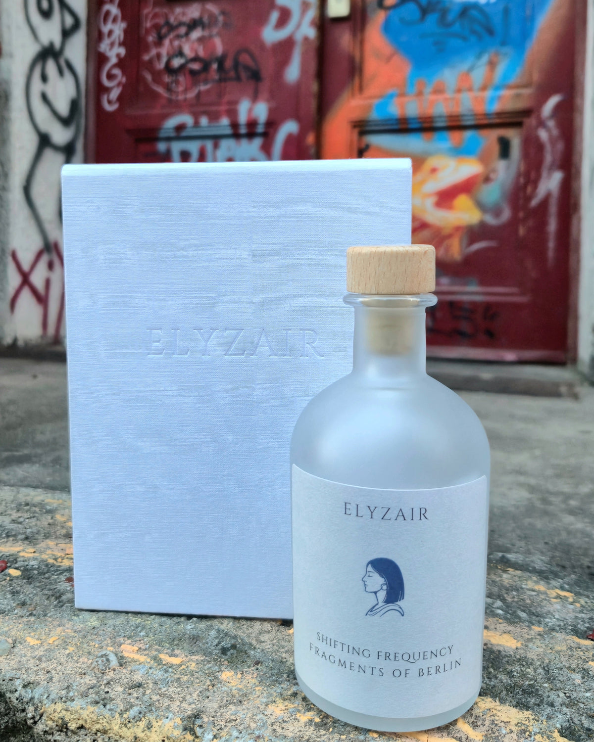 ELYZAIR Shifting Frequency, sealed glass edition of Berlin, with its linen presentation box in front of a graffiti-covered door