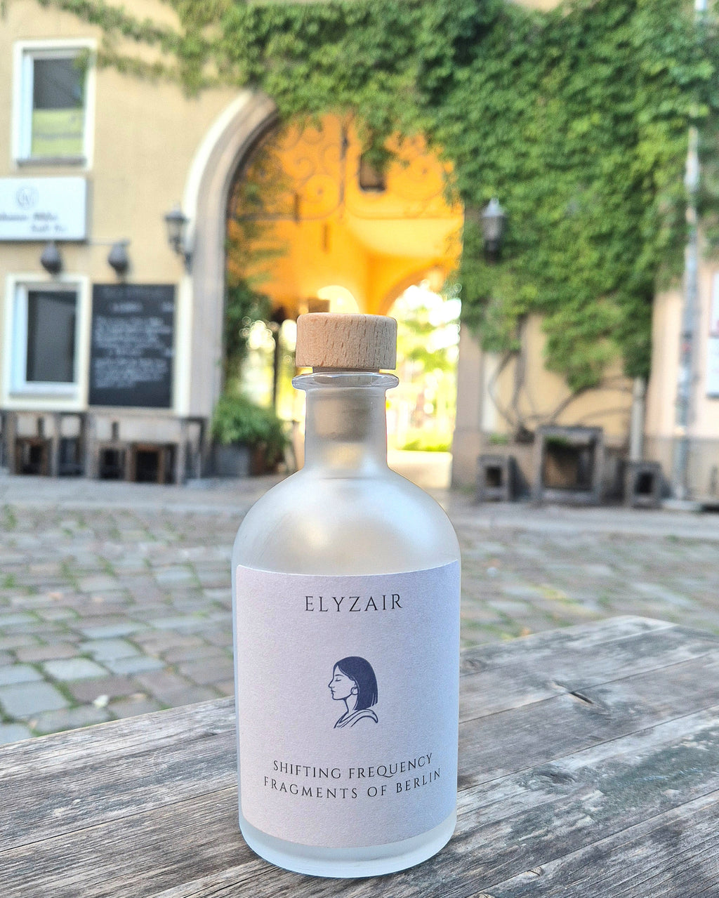 ELYZAIR Shifting Frequency bottle on a weathered wooden table in a cobbled Berlin courtyard